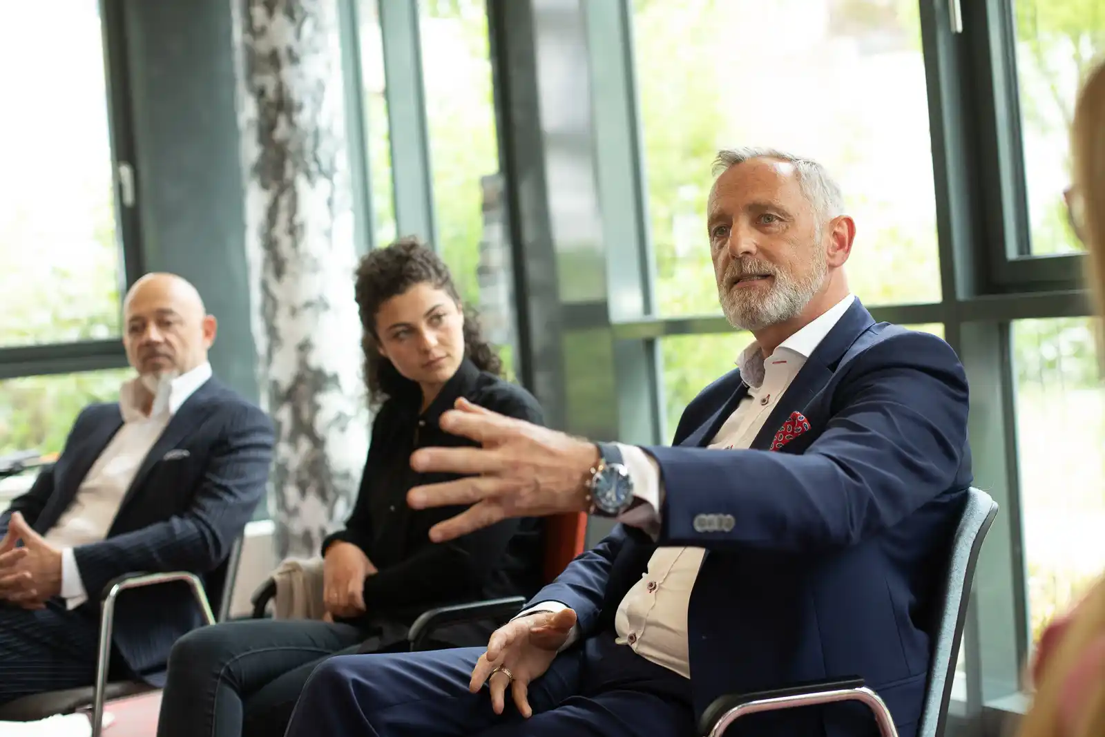 Frank Wiedenmaier spricht während einer Diskussion mit anderen Teilnehmern in einem modernen Raum.