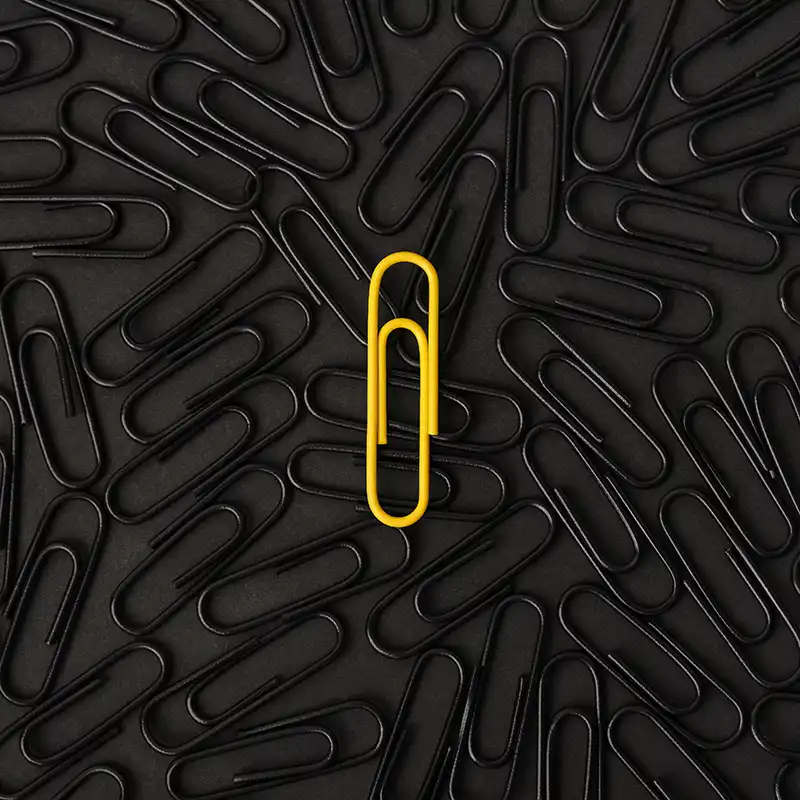 Eine gelbe Büroklammer auf einem Hintergrund aus schwarzen Büroklammern.